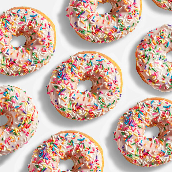 Several donuts with white icing and colorful rainbow sprinkles are arranged on a white background.