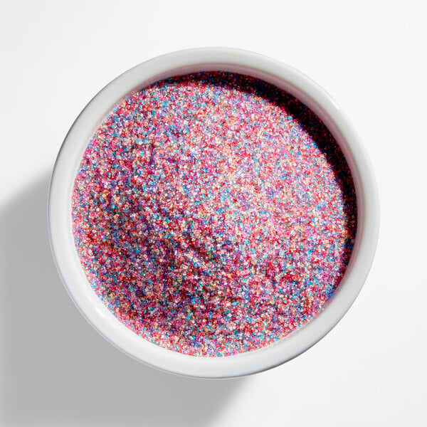 A white bowl filled with fine, multicolored rainbow sanding sugar.