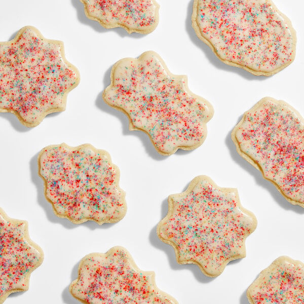 Several frosted cookies with colorful rainbow sanding sugar sprinkles are arranged on a white surface.