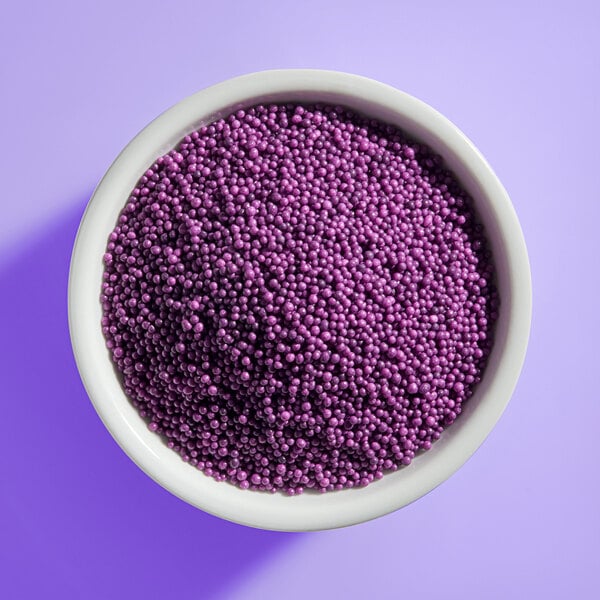 A white bowl filled with small, round, purple beads or sprinkles, viewed from above against a purple background.