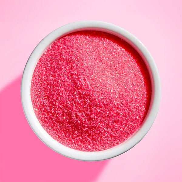 A white bowl filled with bright pink, sparkling granulated sugar on a pink background.