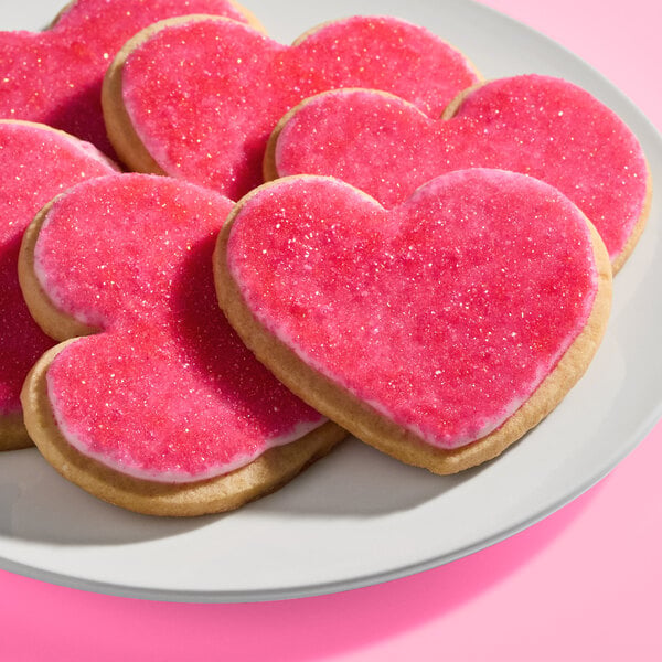 A plate of heart-shaped cookies decorated with pink, sparkly sugar icing.