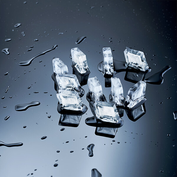 A commercial ice machine producing medium cube ice, shown with several clear ice cubes and water droplets on a reflective surface.