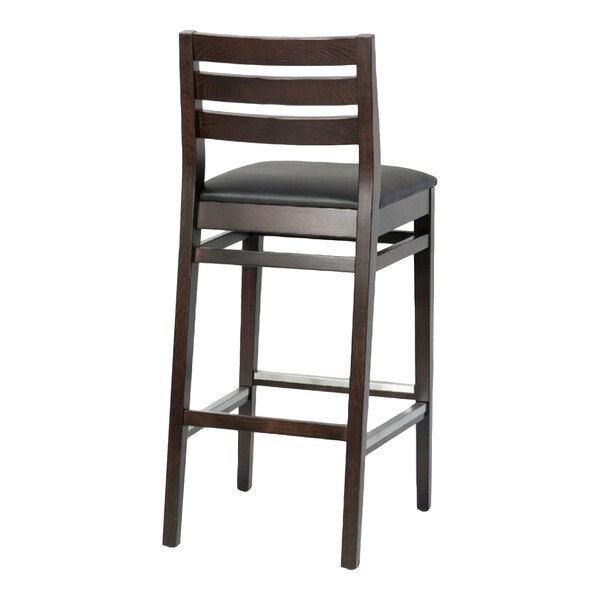 A dark brown beech wood bar stool with a ladder back design and a black faux leather seat.