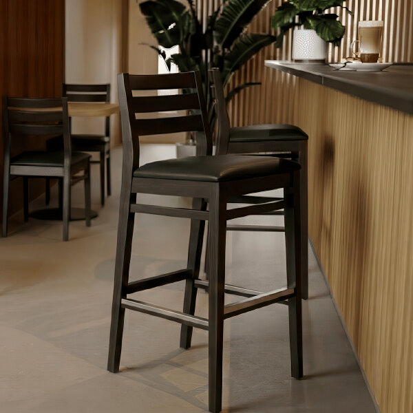 A dark brown beech wood bar stool with a ladder back design and a black faux leather seat.