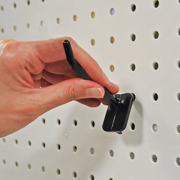 A black polycarbonate locking peg hook being attached to a white pegboard.