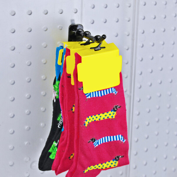 A set of colorful socks with yellow tags hanging on a black polycarbonate locking peg hook attached to a perforated display board.