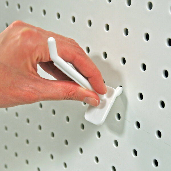 A white polycarbonate locking peg hook being inserted into a perforated pegboard.