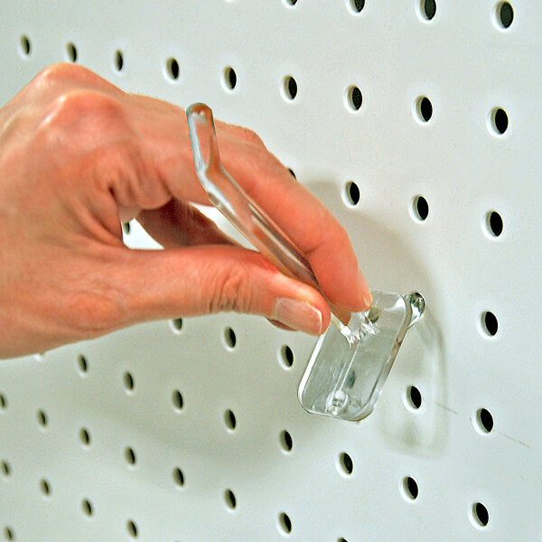 A clear polycarbonate locking peg hook being inserted into a white pegboard.