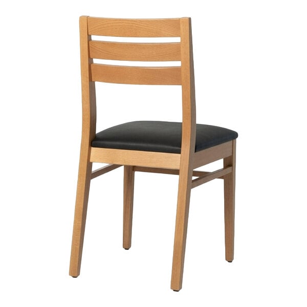 A natural beech wood dining chair with a ladder back design and a black faux leather seat.