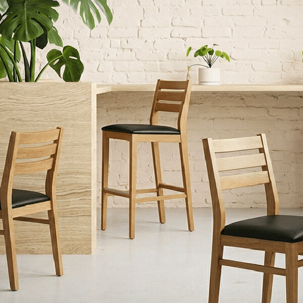 A natural beech wood ladder back bar stool with a black faux leather seat.