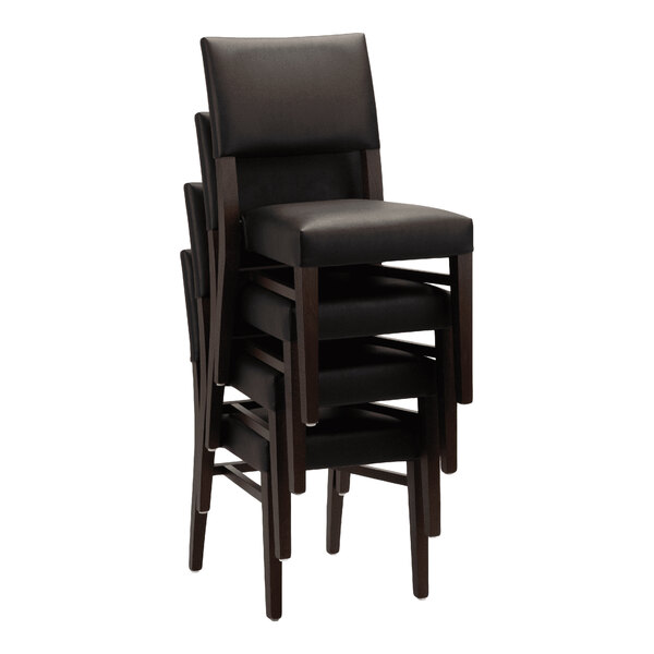 A stack of dark brown beech wood chairs with black faux leather seats and backs.