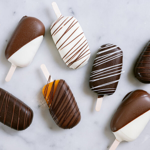 An assortment of chocolate-coated ice cream bars decorated with drizzled chocolate on a marble surface.