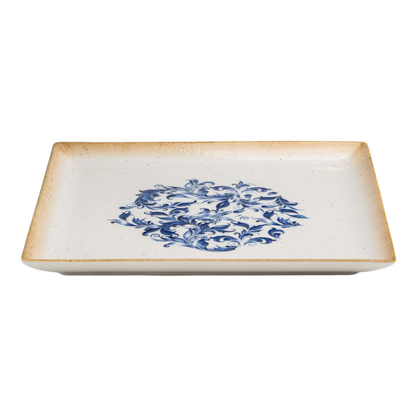A square white porcelain plate with a blue floral design in the center and a tan rim.