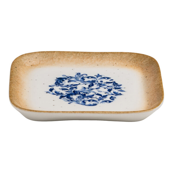 A square white porcelain plate with a blue floral design in the center and a tan rim.