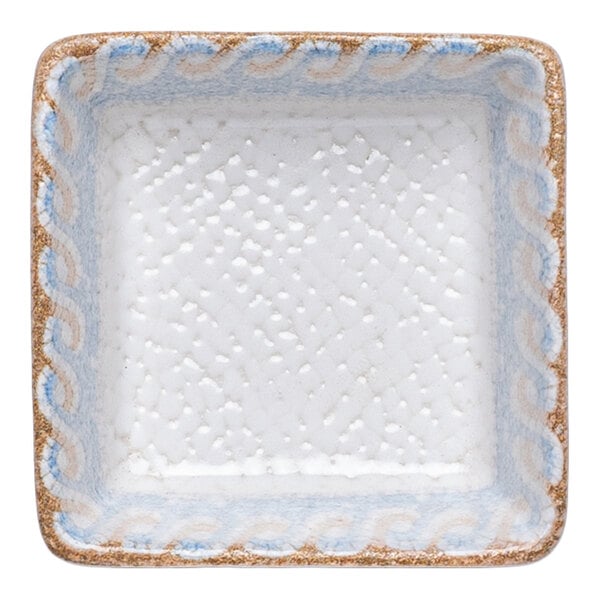 A square white porcelain ramekin with a blue and tan wave design along the rim.