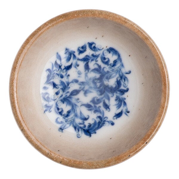 A round white porcelain ramekin with a blue floral design in the center and a tan rim.