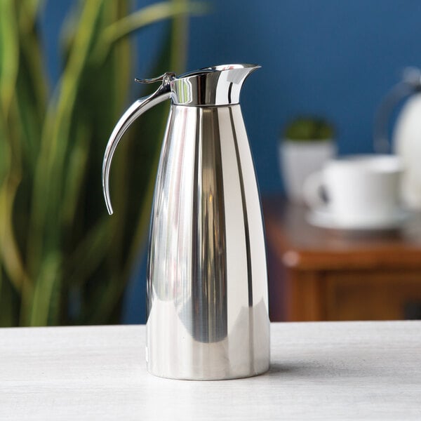 A polished stainless steel insulated coffee carafe with a curved handle and spout.