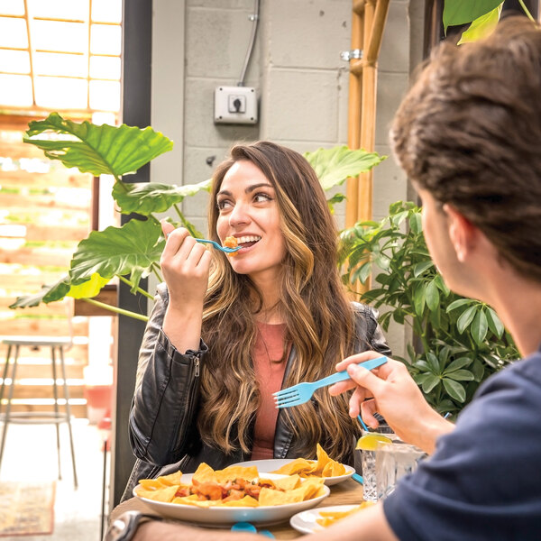 A blue compostable plastic knife being used by a person eating at a table.