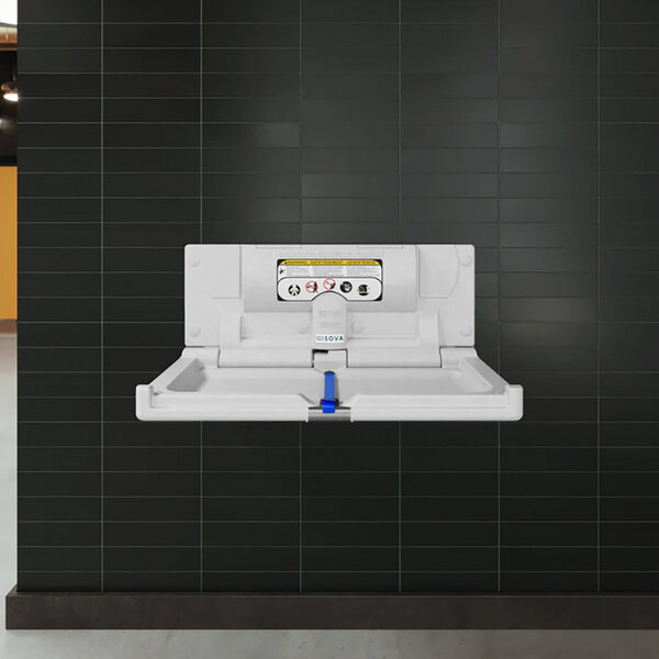 A white granite surface-mount horizontal baby changing station attached to a black tiled wall.
