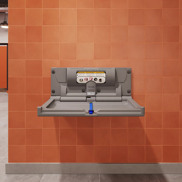 A dark gray surface-mount horizontal baby changing station attached to an orange tiled wall.