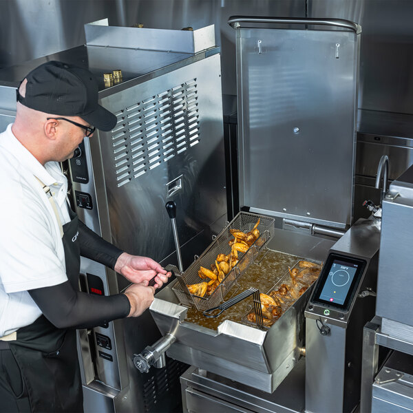 A commercial kitchen worker operating a Cleveland SET-10 10 gallon electric countertop tilt skillet with easyTouch controls, frying food.