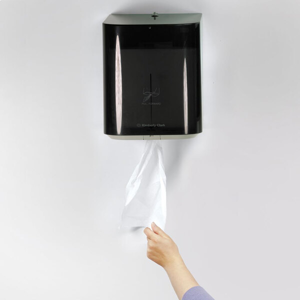 A person is pulling a paper towel from a wall-mounted black dispenser.
