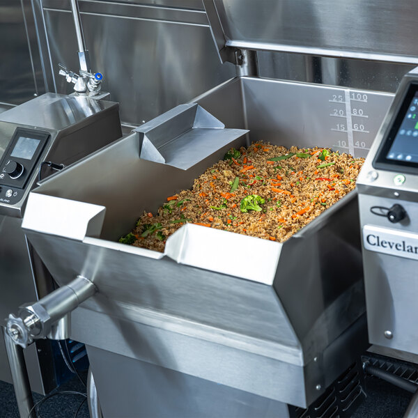 A large stainless steel tilt skillet filled with cooked food, equipped with digital controls and labeled as a Cleveland PowerPan.
