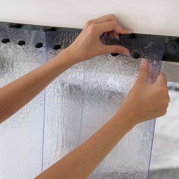 A clear vinyl strip door kit with textured strips being installed onto a black mounting system.