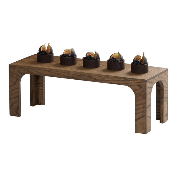 A rectangular chocolate brown oak wood riser with five small desserts displayed on top.