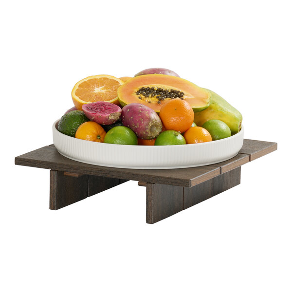 A square mocha-colored HDPE display riser measuring 12 inches by 12 inches by 3 inches, shown holding a bowl of assorted fruit.