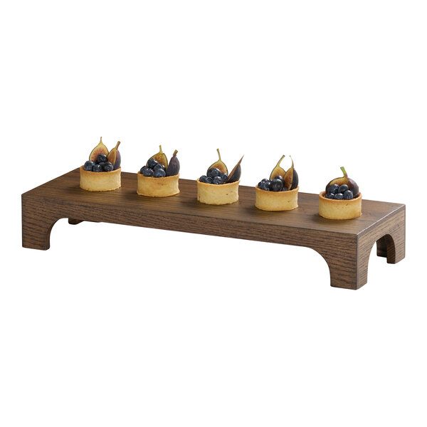 A rectangular chocolate brown oak wood riser with five small fruit tarts displayed on top.