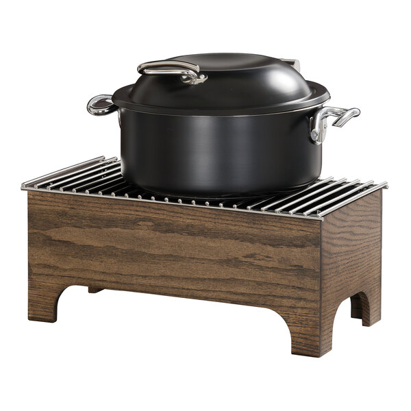 A black pot with a lid sits on a rectangular wooden chafer with a metal grill top.