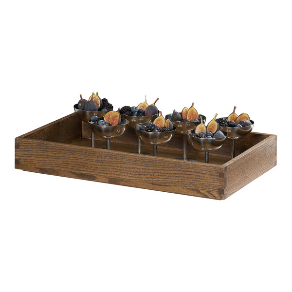 A rectangular oak wood tray holding several glass cups filled with fruit.