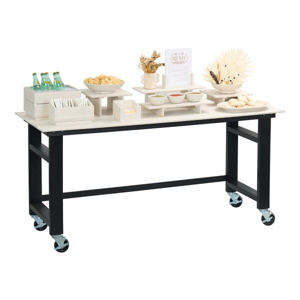 A large rectangular coastal outdoor table or service cart with a light-colored top, black frame, and four casters, shown set up with snacks and drinks.