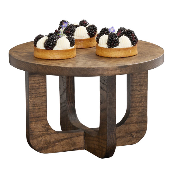 A round chocolate brown oak wood riser with a modern design, shown holding three small desserts.