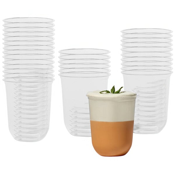 A set of clear, plant-based PLA plastic cold cups with a rounded bottom, shown in multiple stacks and one filled with a layered beverage.