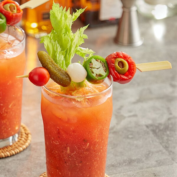 A glass of Bloody Mary garnished with a celery stalk and a bamboo skewer holding a cherry tomato, pickle, cocktail onion, jalapeño slice, and stuffed pepper.
