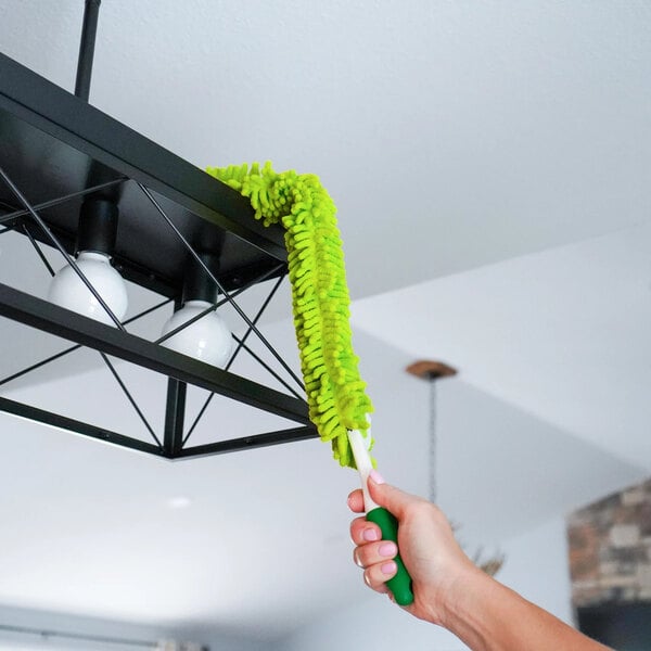 A green flexible microfiber wand duster being used to clean a black light fixture.