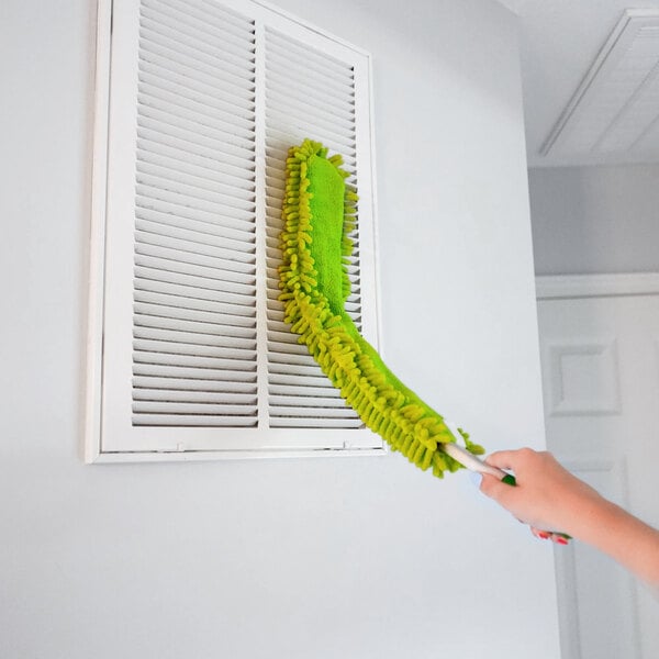 A green flexible microfiber wand duster being used to clean a vent.