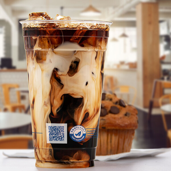 A clear 20 oz. plastic cold cup filled with iced coffee and cream, placed in a café setting.