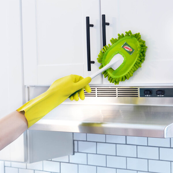 A green microfiber duster with a handle being used to clean a white kitchen cabinet.