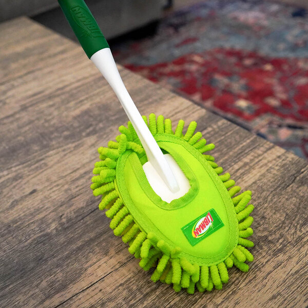 A green Libman microfiber duster with a white handle resting on a wooden surface.