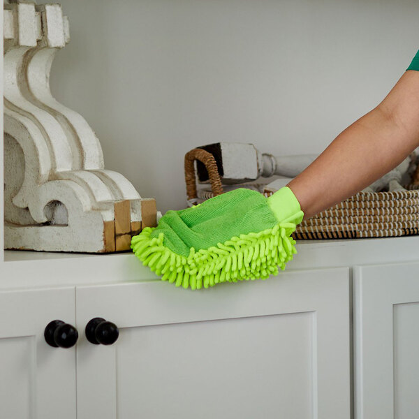 A bright green microfiber duster mitt being used to clean a white cabinet surface.