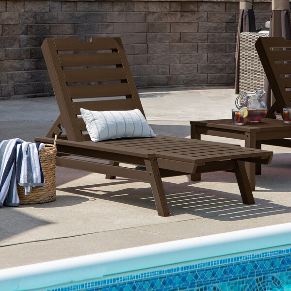 A brown adjustable poly-lumber chaise lounge with a slatted design, positioned beside a pool.
