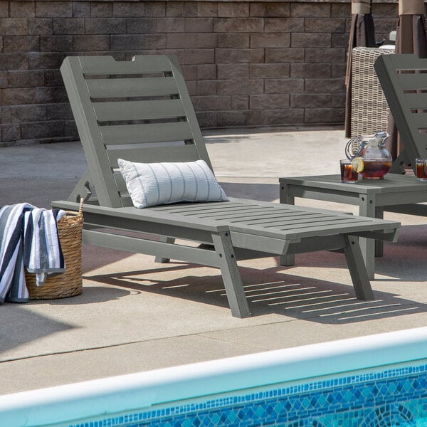A gray adjustable poly-lumber chaise lounge with a slatted design, positioned beside a pool.