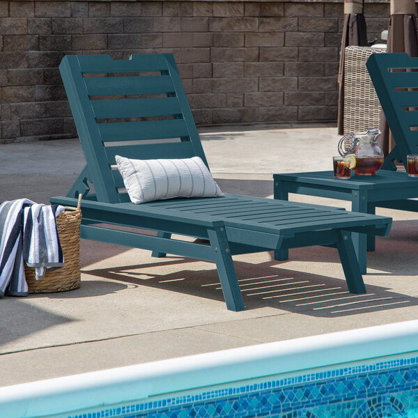 A blue adjustable poly-lumber chaise lounge with a slatted design, positioned beside a pool.