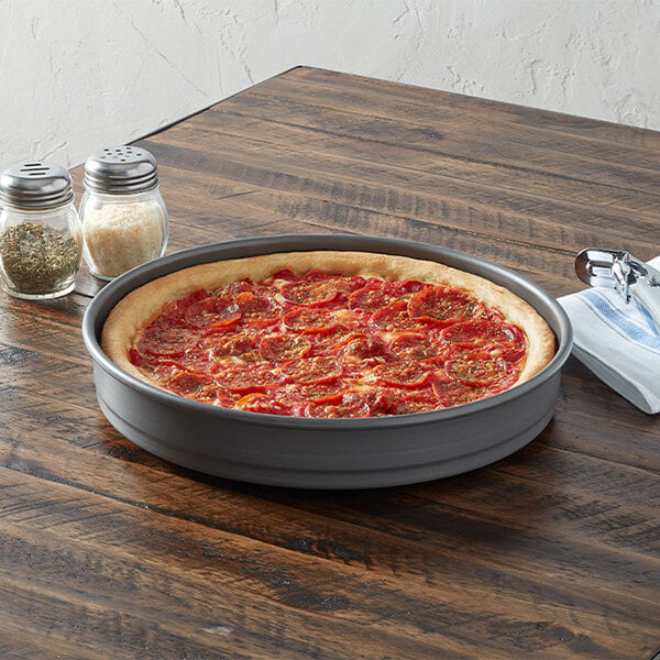 A round, straight-sided aluminum pizza pan containing a deep-dish pizza, placed on a wooden table.