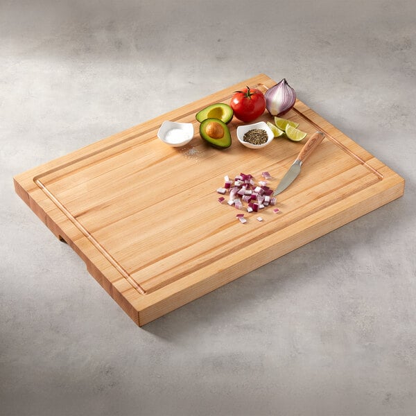 A large rectangular edge grain maple wood cutting board with various chopped and whole ingredients on top.