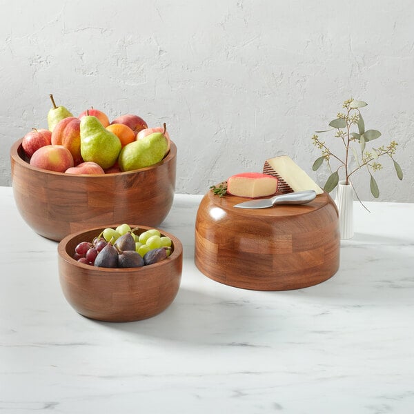 A large round acacia wood bowl with a 120 oz. capacity, shown with fruit inside.